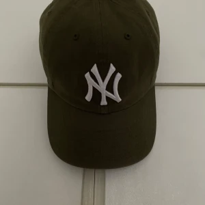 Olivgrön new York Yankees keps  - Snygg olivgrön keps från 47 Brand med en broderad vit logotyp på framsidan. Kepsen har en klassisk design med böjd skärm och justerbar passform. Perfekt för en avslappnad stil. Oanvänd