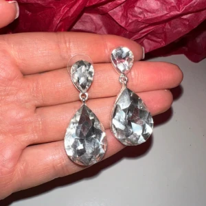 Glittriga silverörhängen - Snygga och glittriga örhängen i silver med stora droppformade kristaller. Perfekta för att ge en extra touch av glamour till din outfit. De har en elegant design som fångar ljuset vackert.