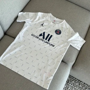 Vit PSG fotbollströja från Jordan - Snygg vit PSG fotbollströja med korta ärmar och diskret mönster av ordet 'Paris'. Tröjan har Jordan-loggan på bröstet och PSG-emblemet. Perfekt för fotbollsfans! Pris går att sänkas!!💯 (vid minsta fundering så hör av dig)