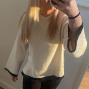 Vit stickad tröja med svarta detaljer och slit på sidorna🩷 - Säljer en stilren vit stickad tröja med svarta kanter vid ärmslut och nederkant. Tröjan har en avslappnad passform och långa ärmar, perfekt för kyligare dagar.