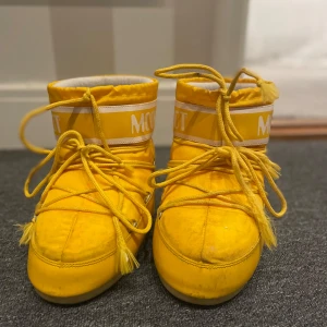 Gula Moon Boots - Snygga och iögonfallande gula Moon Boots med snörning. Perfekta för vintern med sin varma och bekväma design. De har en tydlig logotyp på skaftet och en robust sula för bra grepp. Dom är smutsiga där fram men ska försöka få bort så mycket som möjligt. Skriv för mer bilder. Säljs pågrund av att dom ej används och dom ä försmå🥰