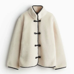 Vit teddyjacka med svarta detaljer - Säljer en mysig vit teddyjacka från H&M med svarta kantdetaljer och knäppning framtill. Jackan har en hög krage och långa ärmar. Den är både stilren och bekväm, ett måste i garderoben! Slutsåld online, hör av er vid frågor❤️ pris kan diskuteras vid snabb affär🥰