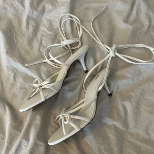 Vita sandaler med klack från ZARA - Eleganta vita sandaler från ZARA med smala remmar och knytning runt ankeln. De har en stilren design med spetsig tå och en liten klack, perfekt för sommarens tillfällen.