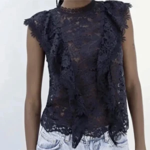 Marinblå spetsblus från Zara  - Snygg svart spetsblus med korta ärmar och ett elegant mönster. Perfekt för att ge en stilfull touch till din outfit. Blusen har en rund hals och är lätt transparent.