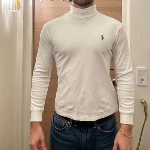 Vit polotröja från Ralph Lauren - Säljer en stilren vit polotröja från Ralph Lauren med det klassiska broderade logotypen på bröstet. Tröjan har långa ärmar och en bekväm passform, perfekt för både vardag och mer uppklädda tillfällen.