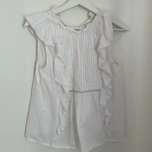 Vit ärmlös blus med volangdetaljer - Säljer en söt vit ärmlös blus med jättefina volangdetaljer. Den är i väldigt fint skicka knappt använd och är köpt från bikbok❤️