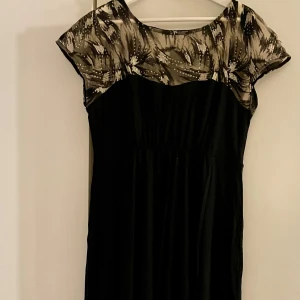 Svart klänning från Tiffany Rose för gravida  - Elegant svart gravidklänning från Tiffany Rose med ett mönstrat överdel i svart och beige. Klänningen har korta ärmar och paljettdekorationer som ger en glittrig effekt. Mycket följsam och skön underkjol. Tillverkad i Storbritannien med en blandning av viskos och elastan för en bekväm passform. Endast använd två gånger. Storleken är 5 men jag uppskattar att den motsvarar en svensk storlek 42.