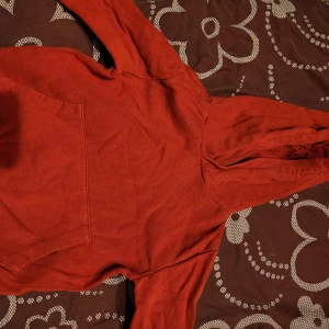 Röd hoodie med ficka - Säljer en röd hoodie med en stor ficka framtill. Perfekt för kyliga dagar och avslappnade stunder. Hoodien har långa ärmar och en bekväm passform.