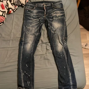 Blå dsquared jeans  - Snygga blå jeans från dsquared med unika färgstänk och slitna detaljer. De har en klassisk femficksdesign och knappgylf. Pris går att diskutera vid snabb affär kvitto finns