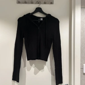 Stickad ziptröja - En svart stickad skottsäkra som slutar ungefär medräknad över höfterna. Använd 1 gång i storlek XS från HM. Har luva och lite längre armar.