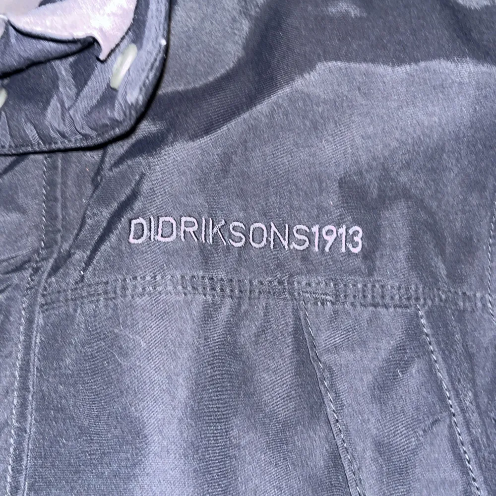Säljer en svart jacka från Didriksons med broderad logga på bröstet. Jackan har dragkedja och knappar framtill samt flera praktiska fickor. Perfekt för kyligare dagar.. Takit.