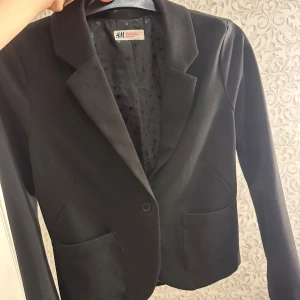 Svart kavaj från H&M - Snygg svart kavaj från H&M med klassisk design. Kavajen har långa ärmar och två fickor framtill. Perfekt för en stilren look.