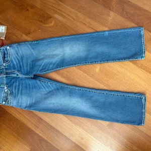 Blå jeansbyxor från True Religion - Snygga blå jeansbyxor från True Religion med en relaxed straight passform. De har gröna broderade detaljer på bakfickorna och en klassisk femficksdesign. Perfekta för en avslappnad stil. Måste lägga till att dem aldrig har blivit använda.