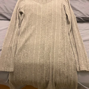 Beige ribbad stickad klänning  - Mysig beige stickad klänning med ribbad struktur. Perfekt för kyliga dagar med sin långa ärmar och bekväma passform. Ett måste i garderoben för en stilren look.Xxl men passar den som har L/xl