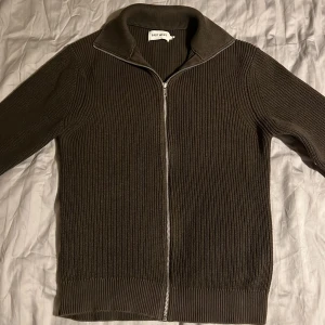 Brun stickad kofta från East West - Säljer en snygg brun stickad kofta från East West med dragkedja framtill. Perfekt för kyliga dagar med sin ribbade design och långa ärmar. En stilren och bekväm tröja för alla tillfällen.
