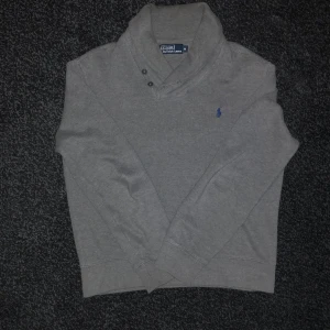 Grå tröja från Polo Ralph Lauren - Säljer en stilren grå tröja från Polo Ralph Lauren med en diskret blå logga på bröstet. Tröjan har en hög krage med knappar och långa ärmar. Perfekt för en avslappnad men ändå snygg look. Endast använd tre gånger. Skicka ett dm om du undrar något! Priset kan diskuteras!