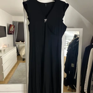 Svart klänning med knyt - Elegant svart klänning med ett stilrent knyt framtill. Klänningen har en smickrande passform och är ärmlös. Aldrig använd 