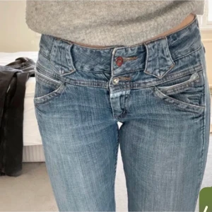 Lowwaisted ljusblåa jeans med unik design - Snygga ljusblå jeans med låg midja och coola detaljer. De har en unik design med dubbla knappar och kontrastsömmar. Jätte snygga!! Säljs pga av att de är för stora. (Bilderna är utav förra ägaren)
