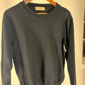 Svart merinoull tröja från Burberry  - Snygg svart tröja från Burberry med diskret broderad logga på bröstet. Tröjan är 50% merinoull och helt utan slitage eller defekter. Tröjan är large men sitter som XS.