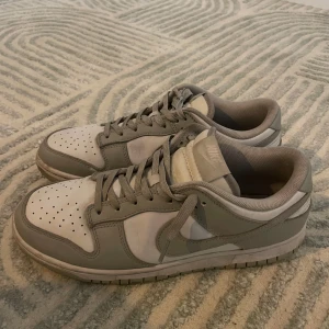 Nike Dunk i grått och vitt - Säljer ett par stilrena Nike Dunk sneakers i grått och vitt. Skorna har klassisk snörning 