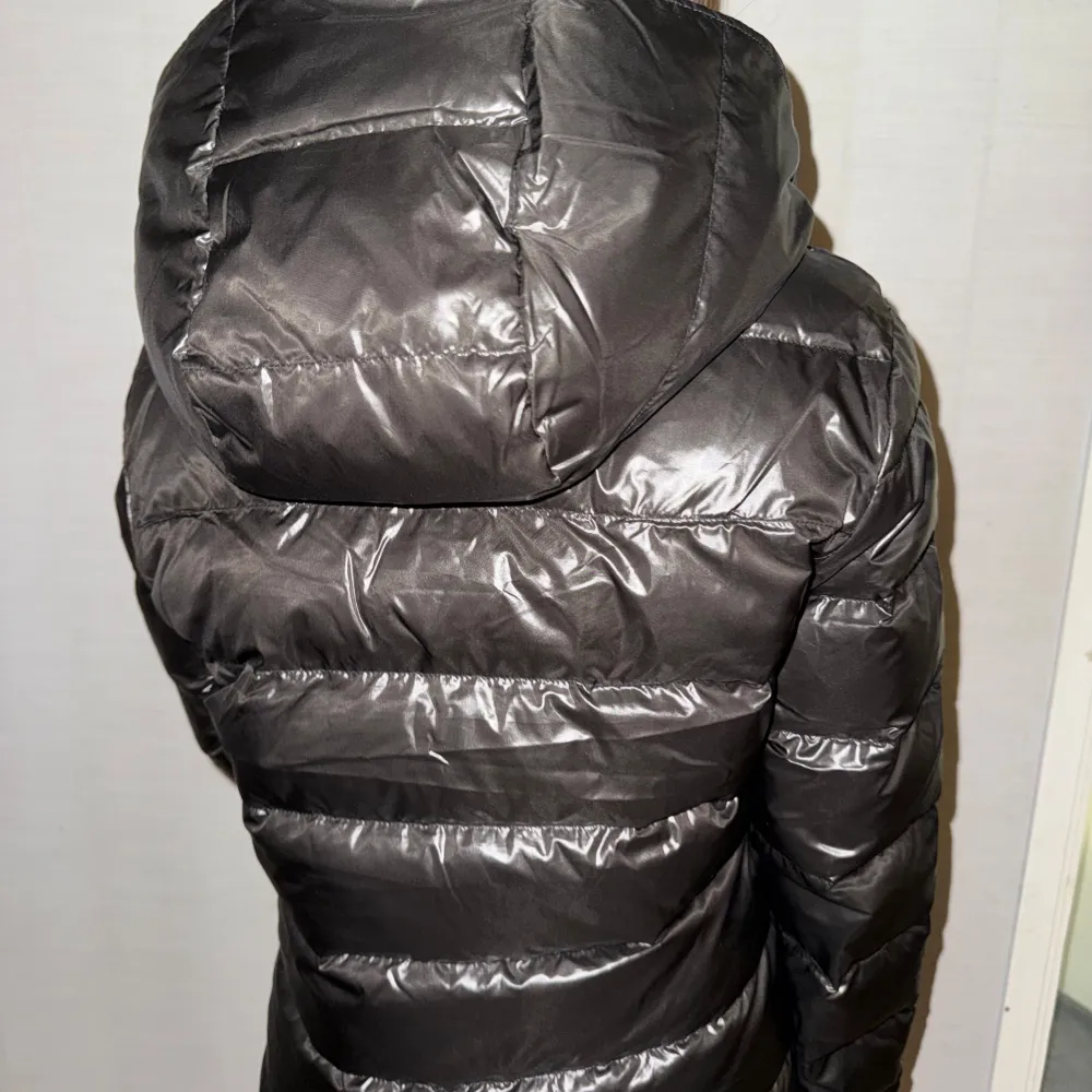 Snygg svart pufferjacka från Massimo Dutti med dragkedja och huva. Perfekt för kyliga dagar med sin stilrena design och bekväma passform.. Takit.