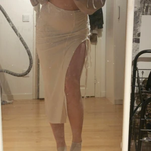 Beige kjol med snörning - Snygg beige kjol med snörning och slits framtill. Kjolen har en tight passform och är perfekt för en stilren look. Den är gjord i ett mjukt material som formar sig fint efter kroppen.