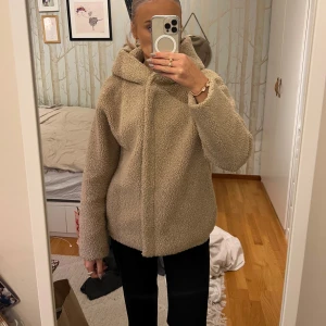 Beige teddyjacka med huva - Mysig beige teddyjacka med huva, perfekt för kyliga dagar. Jackan har en dragkedja framtill och långa ärmar. Den är både stilren och bekväm, vilket gör den till ett utmärkt val för höst och vinter.