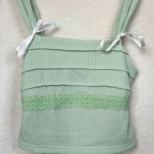 Mint grön topp - Superfin mint grön topp i ribbat material med söta spetsdetaljer. Den har breda axelband med vita rosetter och en knytning i ryggen för en perfekt passform.💚