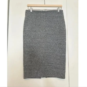 Grå kjol i stickat material - Säljer en stilren grå kjol i stickat material. Den är knälång och har en tight passform som framhäver figuren. Perfekt för både vardag och festliga tillfällen. Superbekväm och lätt att matcha med olika toppar!