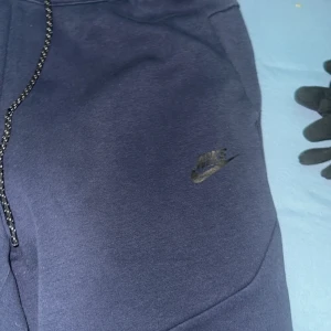 Nike tech marinblå - Säljer ett par  marinblå  Nike tech byxor från Nike i storlek M. Byxorna har en bekväm passform med snörning i midjan och är perfekta för en avslappnad stil. De är tillverkade i mjukt material och har en diskret Nike-logga på sidan. 