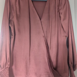 Glansig höstrosa blus - Omlottblus i glansig höstrosa färg med resår i ärmarna. Oanvänd.