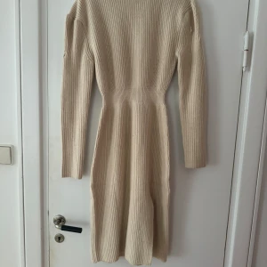 Beige ribbad klänning från ADOORE - Säljer en superfin beige ribbad klänning från ADOORE i storlek 34. Den har en elegant slits och långa ärmar, perfekt för både vardag och fest. Klänningen är i nyskick och har en tight passform som framhäver figuren. Perfekt för höst och vår!