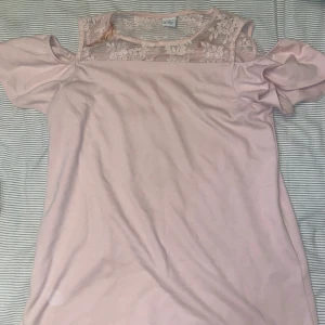Rosa topp med spetsdetaljer från Lindex - Säljer en söt rosa topp från Lindex med spetsdetaljer upptill. Toppen har korta ärmar och en luftig passform, perfekt för sommarens varma dagar. Den är i storlek 158/164, vilket passar barn i åldern 12-14 år.