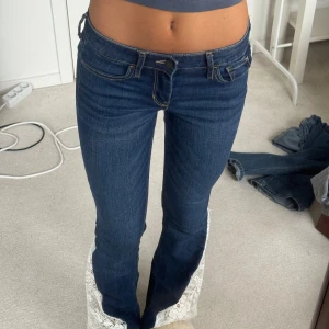 Mörkblå jeans med spetsdetaljer - Säljer ett par snygga mörkblå jeans från Hollister med tillsydda unika spetsdetaljer längst ner på benen som gör de bootcut. De är lågmidjade och har inga defekter 