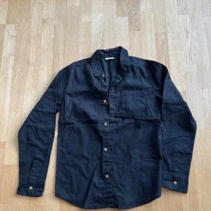 Svart långärmad skjorta - Säljer en stilren svart långärmad skjorta i bomull. Skjortan har knappar framtill och en bröstficka. Perfekt för både vardag och fest! 