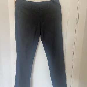 Svarta kostymbyxor från Riley - Säljer ett par stilrena grå kostymbyxor från Riley. De har en klassisk design med raka ben och en knapp i midjan. Perfekta för både formella tillfällen och kontoret. Byxorna är i bra skick och redo för en ny ägare!