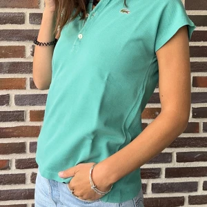 Turkos pikétröja från Lacoste - Säljer en fin mintgrön pikétröja från Lacoste. Den har en klassisk krage med fyra knappar och det ikoniska krokodilmärket på bröstet. Den är vintage och tillverkad i Frankrike. Perfekt för en avslappnad men stilig look. Den är i storlek 36/38