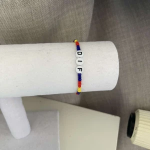 Färgglatt armband med bokstäver - Säljer ett supercoolt armband med bokstäverna 'DIF'. Armbandet är gjort av små pärlor i blått, rött och gult, vilket ger det en härlig och livlig look. Perfekt för att visa ditt stöd eller bara som en färgglad accessoar!