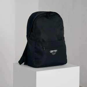 Svart ryggsäck från Aim'n - Säljer en stilren och praktisk svart ryggsäck från Aim'n. Den har en enkel design med en dragkedja framtill och Aim'n-loggan i vitt. Perfekt för vardagsbruk eller träning!