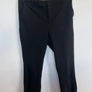 Svarta kostymbyxor från BikBok - Säljer ett par snygga svarta kostymbyxor från BikBok i storlek 44. Byxorna har ett diskret randigt mönster och är perfekta för både jobb och fest. De är tillverkade i ett bekvämt material som känns skönt mot huden. Byxorna har en klassisk passform med raka ben och midwaist. Perfekta för höst och vinter!