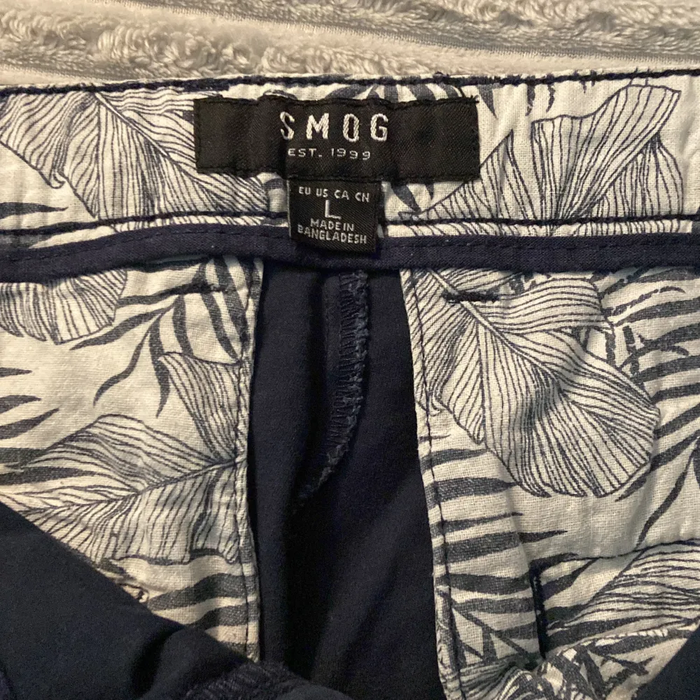 Säljer ett par snygga mörk blåa shorts från SMOG i storlek L. De är perfekta för sommaren och har en klassisk design med två framfickor och två bakfickor. Materialet känns som bomull och de har en knapp och dragkedja framtill. Perfekta för både vardag och avslappnade tillfällen!. Shorts.