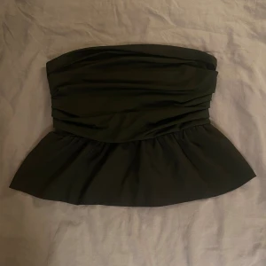 Svart tubtopp med volang - Säljer en snygg svart tubtopp med volangdetaljer. Toppen är axelbandslös och har en tight passform som framhäver figuren. Perfekt för festliga tillfällen eller en utekväll❤️.