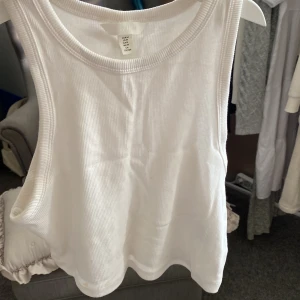 Vit ribbad linnetopp från H&M - Säljer en vit ribbad linnetopp från H&M. Den är ärmlös och perfekt för sommaren. Toppen är i storlek M och är gjord av ett mjukt och bekvämt material. Perfekt för en avslappnad och stilren look! köparen betalar för frakt 