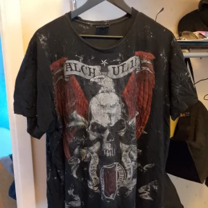 Svart t-shirt med dödskalletryck - Säljer en svart t-shirt med ett coolt dödskalletryck på framsidan. T-shirten har korta ärmar och är i välanvänt skick med en del slitage och färgfläckar. Perfekt för en rockig look eller för avslappnade dagar. Passar bra till jeans eller shorts.