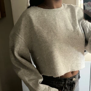 Grå croppad sweatshirt - Säljer en superfin grå croppad sweatshirt. Den är perfekt för en avslappnad look och passar till både jeans och leggings eller över klänning/kjol. Tröjan är långärmad och har en normal passform. Materialet är mjukt och bekvämt, perfekt för höst och vår. Super fin eftersom den har lite ballong ärmar. Den är i nyskick och knappt använd. Perfekt för en chill dag eller en casual utflykt. 🩶