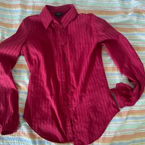 Röd skjorta från Lindex - Säljer en snygg röd skjorta från Lindex i storlek 38. Skjortan har ett randigt mönster och är långärmad med knappar hela vägen ner. Perfekt för både vardag och fest! 💃