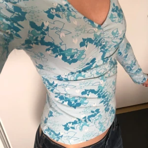 Blå långärmad topp med blommigt mönster - 🎀Superfin blå långärmad topp med ett blommigt mönster. | V-ringad hals och söta rosetter vid ärmsluten | Köpt secondhand, använd en gång! 🎀