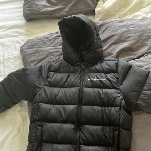 Svart dunjacka från Sail Racing - Säljer en svart dunjacka från Sail Racing i storlek herr M. Jackan är i nyskick och har en normal passform. Den har en dragkedja framtill och en huva för extra skydd mot kyla. Perfekt för vintern!  Köpt på Vingåker outlet för 2800   Mörkblå / svart