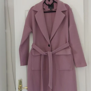 Ljuslila kappa från Amisu - Säljer en superfin ljuslila kappa från Amisu i storlek 36. Den har en klassisk design med en knäppning framtill och ett bälte i midjan för en snygg passform. Kappan har långa ärmar och två stora fickor fram. Perfekt för höst. Den är nobbrig, vilket kan tas bort med borttagare, därav priset. Annars väldigt fin 💜