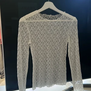 Vit spetsblus - Säljer en vit spetsblus med långärmad design. Blusen är tillverkad av ett vackert spetsmaterial som ger en romantisk och feminin känsla. Perfekt för både vardag och festliga tillfällen. Blusen är i nyskick och har en tight passform.